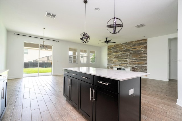 15586 Hamlin Blossom Ave, Winter Garden, FL 34787 - kitchen with a ceiling fan, dark cabinets, decorative light fixtures, a kitchen island, and light wood-style flooring