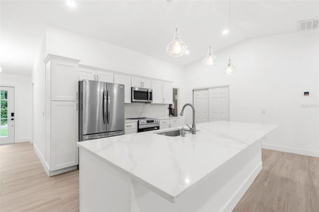 4527 Bamonte St, North Port, FL 34286 - kitchen with stainless steel appliances, white cabinets, an island with sink, light wood finished floors, and vaulted ceiling