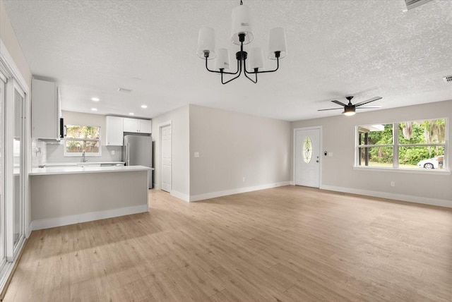 213 Flagler Ave, Edgewater, FL 32132 - unfurnished living room with a textured ceiling, light wood-type flooring, a ceiling fan, a chandelier, and healthy amount of natural light