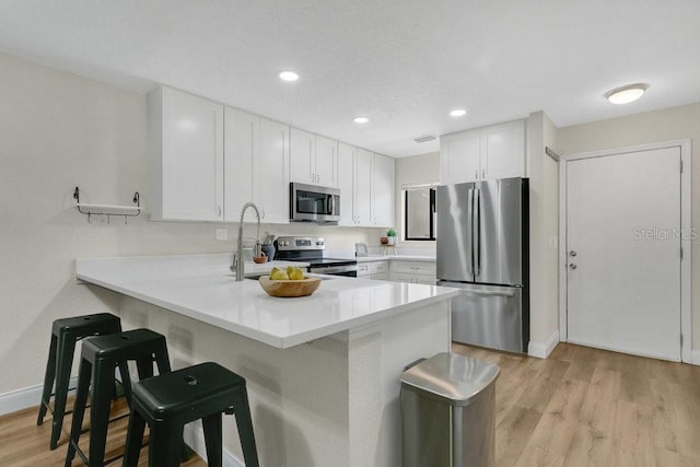 2318 Inagua Way, Winter Park, FL 32792 - kitchen featuring stainless steel appliances, a breakfast bar, a peninsula, white cabinetry, and light wood finished floors