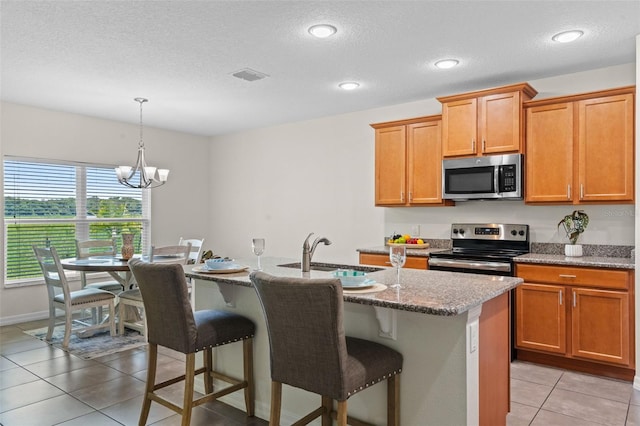1330 Bucktail Ct, Kissimmee, FL 34746 - kitchen featuring appliances with stainless steel finishes, a breakfast bar area, a kitchen island with sink, stone counters, and a textured ceiling