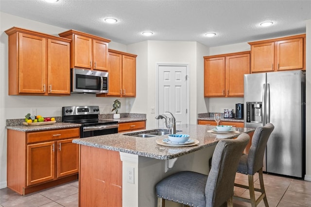 1330 Bucktail Ct, Kissimmee, FL 34746 - kitchen with stainless steel appliances, light tile patterned flooring, a kitchen bar, an island with sink, and light stone counters