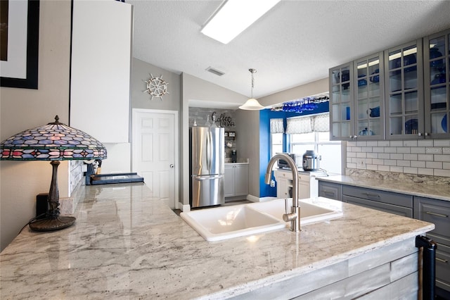 1145 Jaybee Ave, Davenport, FL 33897 - kitchen featuring freestanding refrigerator, glass insert cabinets, lofted ceiling, light stone countertops, and decorative light fixtures