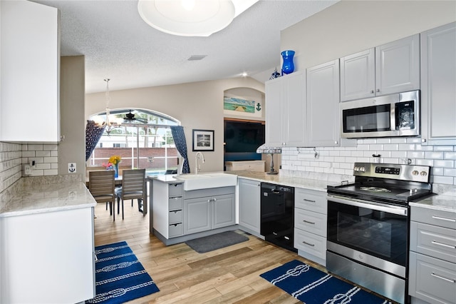 1145 Jaybee Ave, Davenport, FL 33897 - kitchen featuring appliances with stainless steel finishes, light wood-style floors, a peninsula, tasteful backsplash, and lofted ceiling