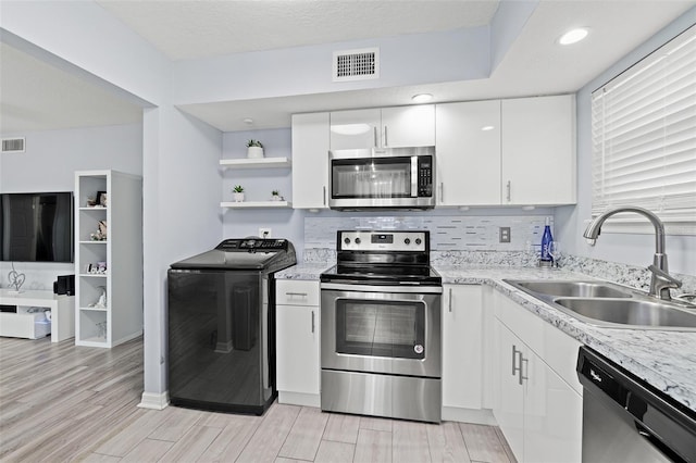 kitchen with stainless steel appliances, washer / clothes dryer, white cabinets, open shelves, and light wood-style flooring
