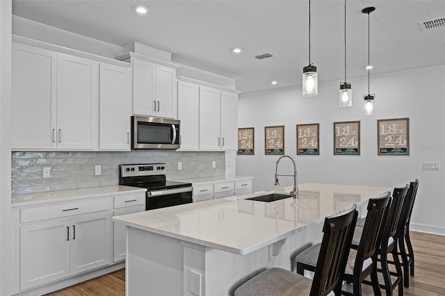 2936 Wild Mulberry Dr, Clermont, FL 34711 - kitchen with appliances with stainless steel finishes, light wood finished floors, a kitchen island with sink, decorative backsplash, and recessed lighting