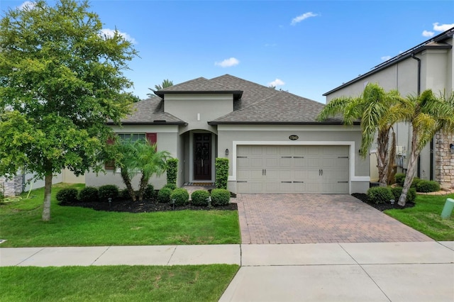 17242 Hickory Wind Dr, Clermont, FL 34711 - view of front of home with stucco siding, decorative driveway, a front lawn, roof with shingles, and an attached garage