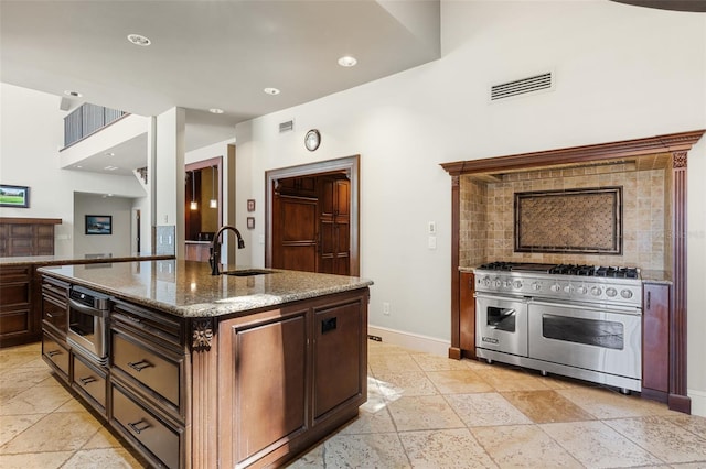 10545 Down Lakeview Cir, Windermere, FL 34786 - kitchen featuring range with two ovens, light stone counters, stone tile flooring, an island with sink, and recessed lighting