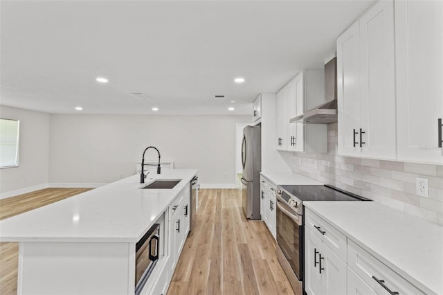 671 25th St SW, Largo, FL 33770 - kitchen with appliances with stainless steel finishes, wall chimney range hood, a center island with sink, light wood finished floors, and decorative backsplash