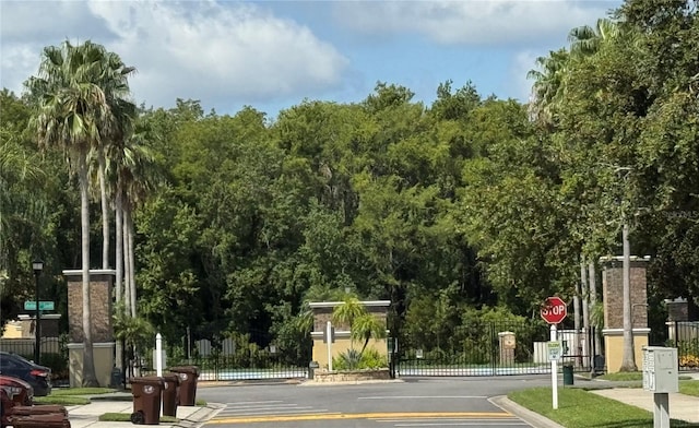 3069 Ashland Ln N, Kissimmee, FL 34741 - view of asphalt road featuring traffic signs, curbs, a gate, sidewalks, and street lights