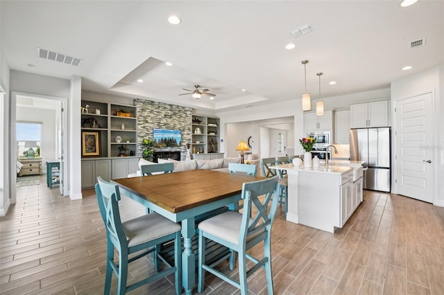 17838 Hither Hills Cir, Winter Garden, FL 34787 - dining space featuring a tray ceiling, a stone fireplace, recessed lighting, light wood-type flooring, and a ceiling fan