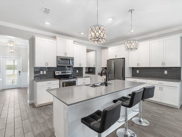 2452 Camden Park Ave, Davenport, FL 33837 - kitchen featuring appliances with stainless steel finishes, ornamental molding, a chandelier, an island with sink, and wood tiled floors