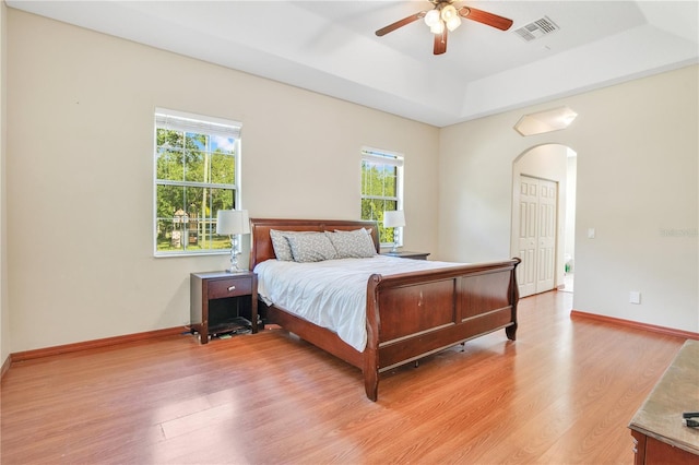 18852 Starry St, Orlando, FL 32833 - bedroom featuring arched walkways, multiple windows, a tray ceiling, and light wood-style flooring
