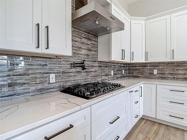 1329 Jumana Loop, Apollo Beach, FL 33572 - kitchen with black gas cooktop, ventilation hood, backsplash, white cabinets, and light stone counters