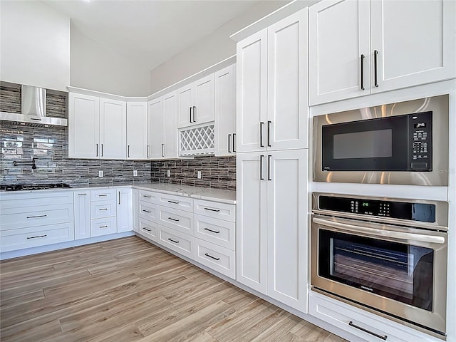 1329 Jumana Loop, Apollo Beach, FL 33572 - kitchen featuring appliances with stainless steel finishes, wall chimney range hood, white cabinets, and decorative backsplash