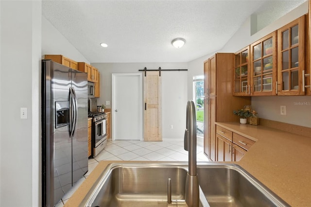 2212 Clementine Trl, Clermont, FL 34714 - kitchen featuring stainless steel appliances, brown cabinets, a barn door, a textured ceiling, and glass insert cabinets