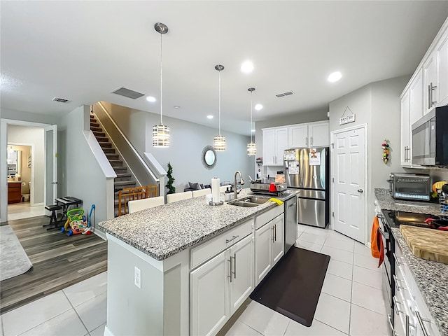 1808 Regal River Cir, Ocoee, FL 34761 - kitchen featuring appliances with stainless steel finishes, light tile patterned flooring, white cabinets, light stone countertops, and a center island with sink