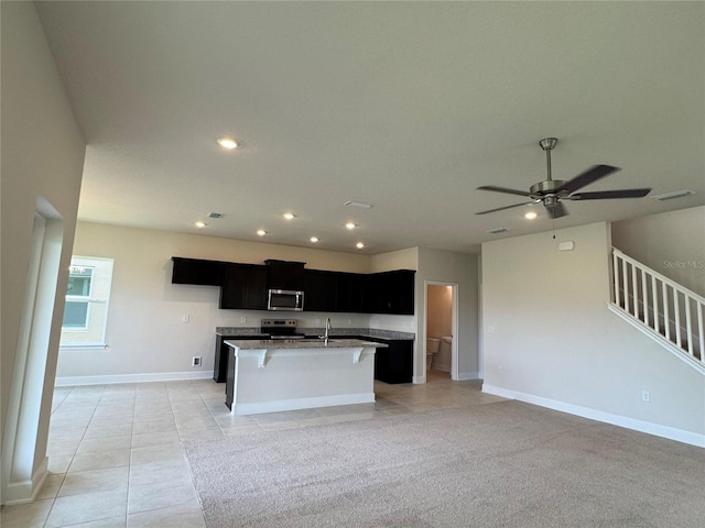 4101 Sagefield Dr, Harmony, FL 34773 - kitchen with stainless steel appliances, dark cabinetry, open floor plan, a kitchen island with sink, and a ceiling fan