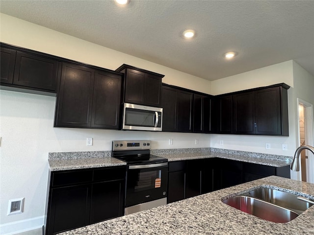 4101 Sagefield Dr, Harmony, FL 34773 - kitchen with appliances with stainless steel finishes, light stone counters, a textured ceiling, recessed lighting, and dark cabinets