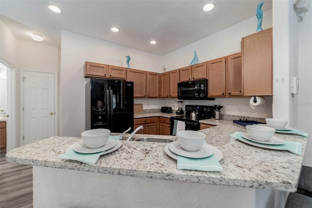 2792 Roccella Ct, Kissimmee, FL 34747 - kitchen with black appliances, a peninsula, light wood-style flooring, brown cabinetry, and light stone counters