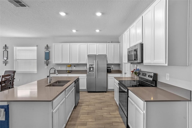4491 Holstein St, Saint Cloud, FL 34772 - kitchen with appliances with stainless steel finishes, a textured ceiling, light wood-type flooring, white cabinetry, and a center island with sink
