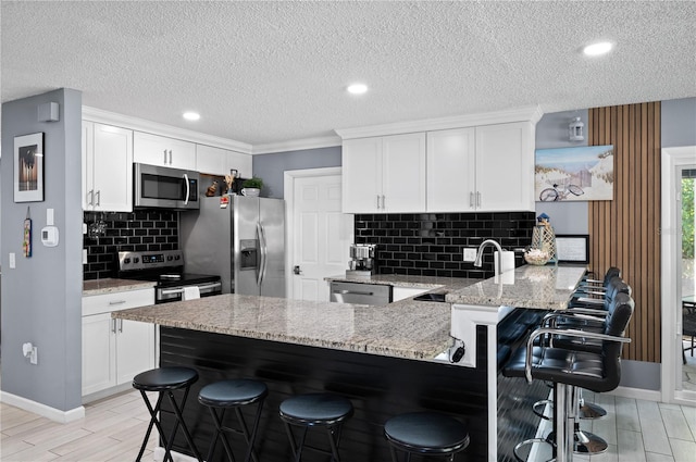 874 Acadia Rd, Venice, FL 34293 - kitchen with stainless steel appliances, a peninsula, decorative backsplash, wood finish floors, and white cabinets