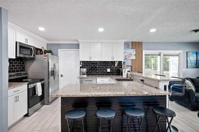 874 Acadia Rd, Venice, FL 34293 - kitchen featuring appliances with stainless steel finishes, a peninsula, a breakfast bar area, a textured ceiling, and decorative backsplash
