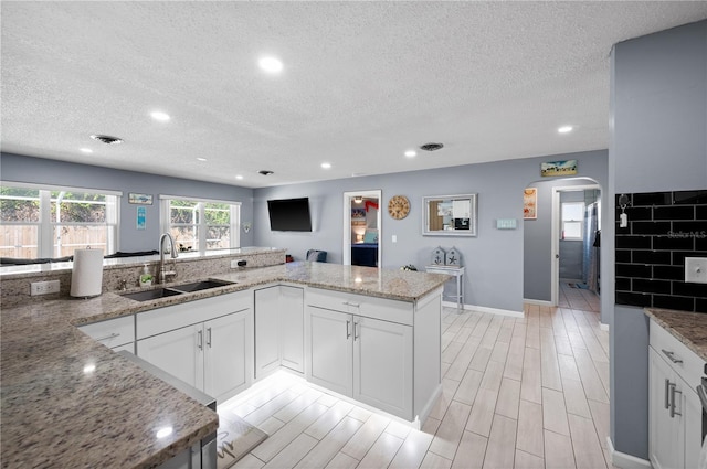 874 Acadia Rd, Venice, FL 34293 - kitchen featuring a textured ceiling, light stone countertops, recessed lighting, arched walkways, and white cabinetry