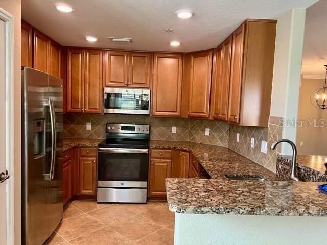 20080 Ragazza Cir Unit 102, Venice, FL 34293 - kitchen with stainless steel appliances, brown cabinetry, a peninsula, dark stone countertops, and recessed lighting