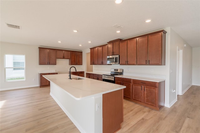 3840 Fescue St, Clermont, FL 34714 - kitchen with stainless steel appliances, light wood-style floors, a center island with sink, brown cabinetry, and recessed lighting