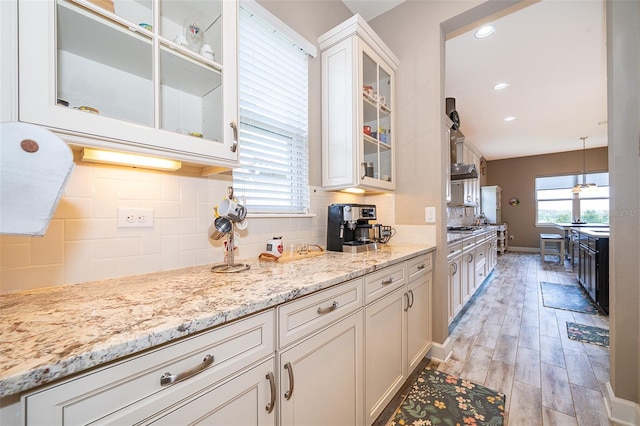 3546 Mediterra Dr, Clermont, FL 34711 - kitchen featuring white cabinetry, decorative backsplash, light stone countertops, glass insert cabinets, and light wood finished floors