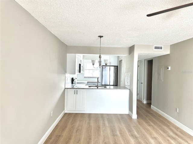 6054 Amberly Ct Unit T21, Orlando, FL 32822 - kitchen featuring freestanding refrigerator, a textured ceiling, a chandelier, light wood-type flooring, and white cabinets