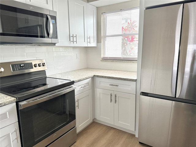 6054 Amberly Ct Unit T21, Orlando, FL 32822 - kitchen with appliances with stainless steel finishes, white cabinetry, light wood-style floors, decorative backsplash, and light stone counters