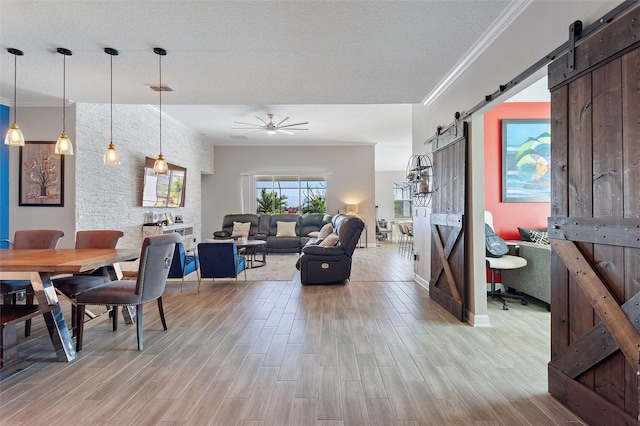 8998 Croquet Ct, Champions Gate, FL 33896 - dining room featuring a barn door, light wood finished floors, ornamental molding, ceiling fan, and a textured ceiling