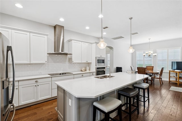 16415 Good Hearth Blvd, Clermont, FL 34711 - kitchen with wall chimney exhaust hood, appliances with stainless steel finishes, tasteful backsplash, an island with sink, and a kitchen bar