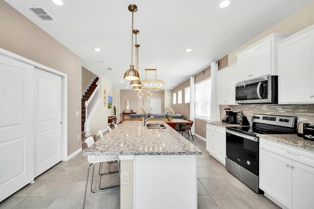 3448 Lilac Way, Davenport, FL 33897 - kitchen featuring stainless steel appliances, tasteful backsplash, light tile patterned flooring, a kitchen island with sink, and white cabinetry