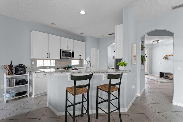 11337 Via Andiamo, Windermere, FL 34786 - kitchen featuring stainless steel microwave, arched walkways, a textured ceiling, a kitchen bar, and white cabinetry