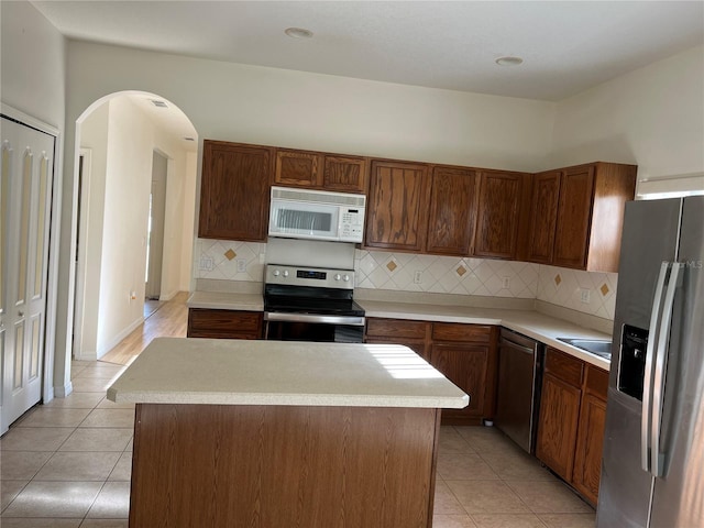 7714 Tanbier Dr, Orlando, FL 32818 - kitchen with stainless steel appliances, arched walkways, light tile patterned flooring, light countertops, and decorative backsplash