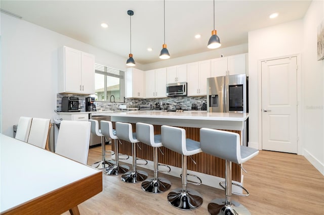 2813 Sanctuary Dr, Clermont, FL 34714 - kitchen featuring stainless steel appliances, tasteful backsplash, light wood-type flooring, white cabinetry, and a breakfast bar