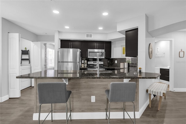 7350 Westpointe Blvd Unit 215, Orlando, FL 32835 - kitchen featuring appliances with stainless steel finishes, dark cabinetry, a kitchen bar, dark stone countertops, and backsplash
