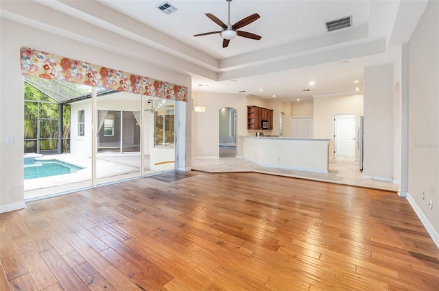 2317 Warren Woods Dr, Orlando, FL 32835 - unfurnished living room featuring a tray ceiling, ceiling fan, arched walkways, light wood finished floors, and recessed lighting