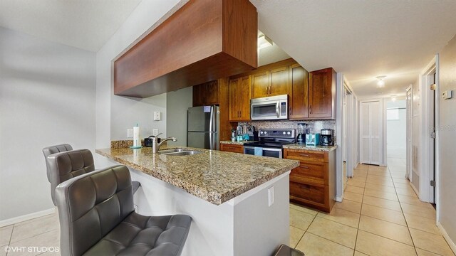 3151 Britannia Blvd Unit A, Kissimmee, FL 34747 - kitchen with stainless steel appliances, light tile patterned floors, a peninsula, backsplash, and light stone countertops