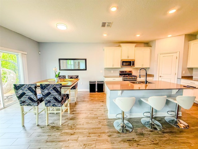 1047 Oak Bluff Dr, Davenport, FL 33837 - kitchen with stainless steel appliances, light wood-style flooring, white cabinetry, an island with sink, and a kitchen breakfast bar