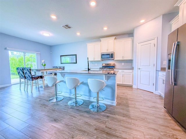 1047 Oak Bluff Dr, Davenport, FL 33837 - kitchen with stainless steel appliances, white cabinets, a kitchen bar, light wood finished floors, and recessed lighting