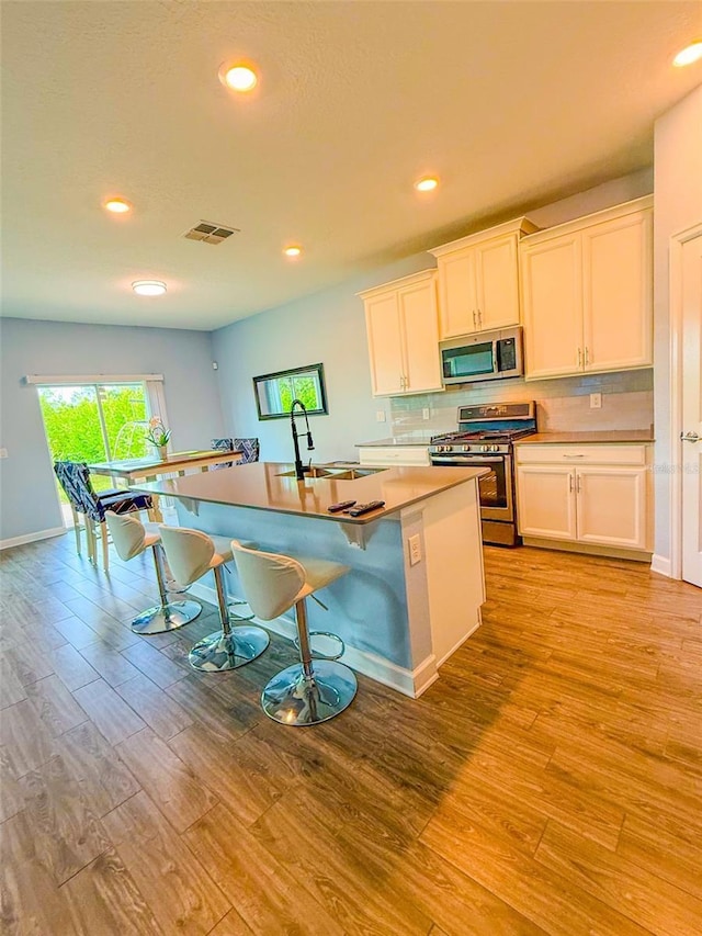 1047 Oak Bluff Dr, Davenport, FL 33837 - kitchen with appliances with stainless steel finishes, light wood-type flooring, a center island with sink, recessed lighting, and a breakfast bar area