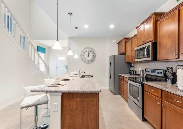 8874 Qin Loop, Kissimmee, FL 34747 - kitchen with stainless steel appliances, a breakfast bar, brown cabinetry, tasteful backsplash, and an island with sink