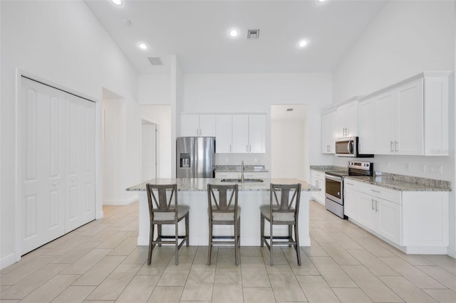 2912 SW Savona Blvd, Port St Lucie, FL 34953 - kitchen featuring appliances with stainless steel finishes, a breakfast bar area, white cabinetry, a kitchen island with sink, and light stone counters