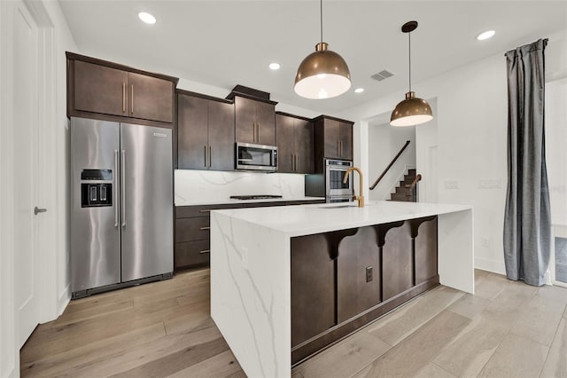 7412 Estuary Lake Loop, Celebration, FL 34747 - kitchen featuring appliances with stainless steel finishes, light wood-type flooring, a kitchen island with sink, dark brown cabinets, and a breakfast bar area