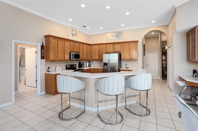 1331 Marble Crest Way, Winter Garden, FL 34787 - kitchen featuring appliances with stainless steel finishes, arched walkways, light tile patterned floors, brown cabinetry, and ornamental molding