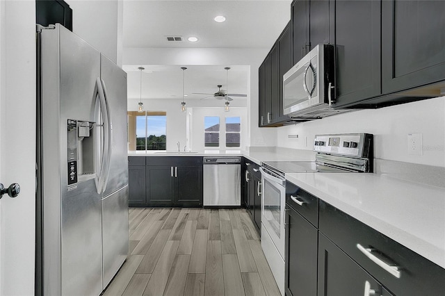 17458 Chateau Pine Way, Clermont, FL 34711 - kitchen featuring appliances with stainless steel finishes, a ceiling fan, dark cabinetry, light countertops, and light wood-type flooring